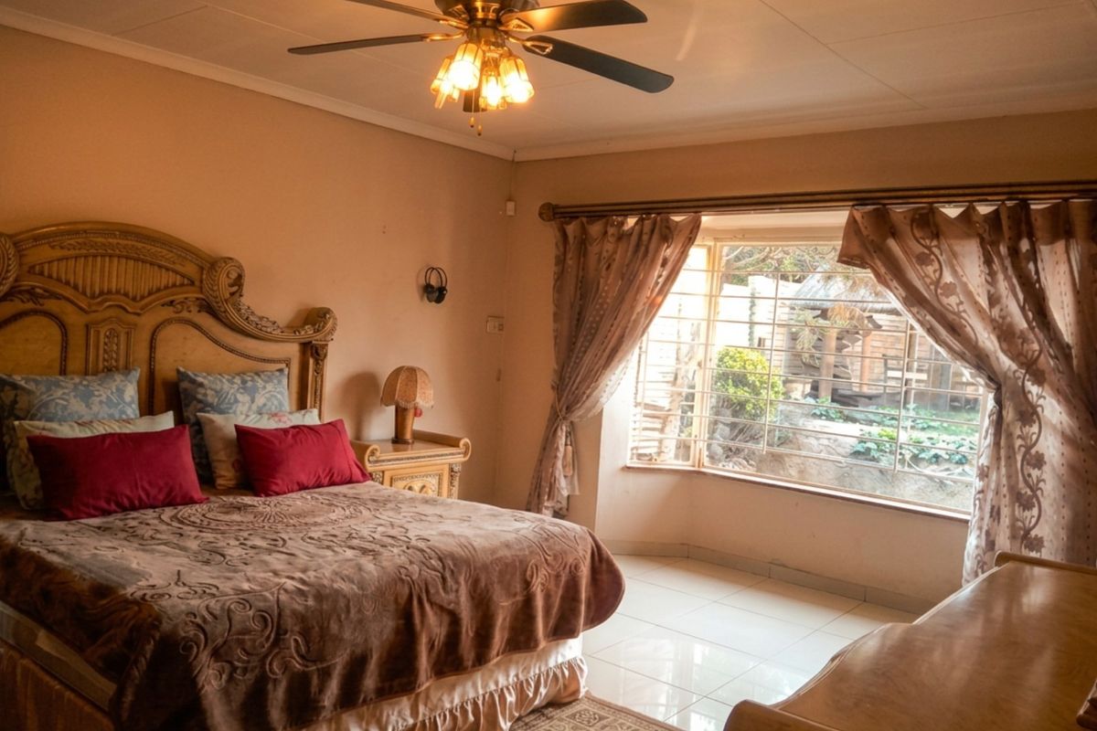 A spacious bedroom featuring tiled flooring, a ceiling fan, and a large bay window with security bars overlooking the garden.