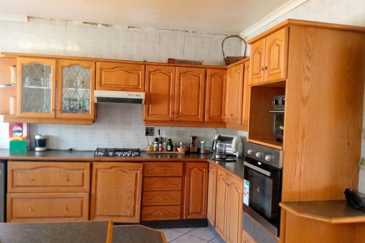 A dated kitchen featuring traditional wooden cabinetry, built-in oven, gas hob, and tiled backsplash, offering potential for a modern renovation.