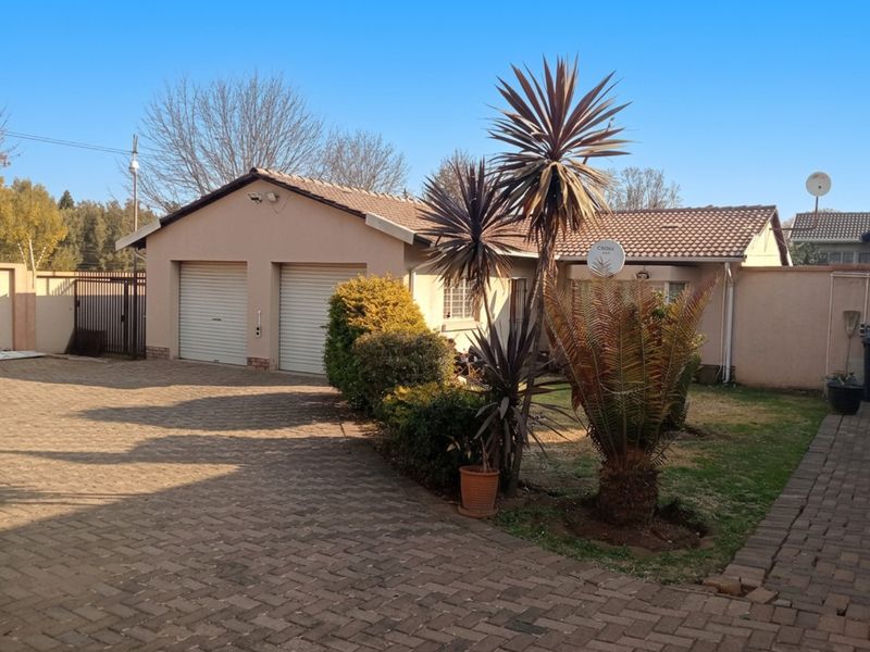 Front view of a residential property featuring a double garage, paved driveway, and established garden with boundary walling.