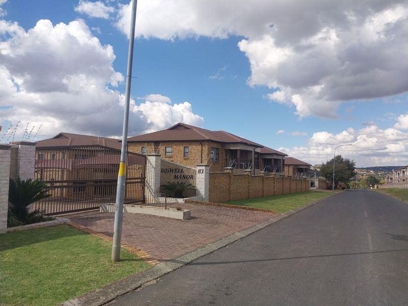 Street view of Boswell Manor, featuring a secure face brick apartment complex with paved driveway, perimeter walling, and electric fencing.