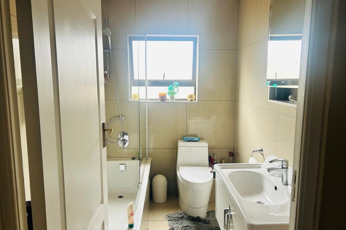 A compact, well-maintained bathroom featuring a bathtub with a glass screen, a modern vanity unit, and neutral wall tiling.