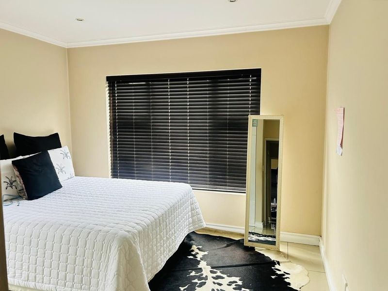 A well-maintained bedroom featuring neutral wall tones, tiled flooring, recessed downlighting, and dark venetian blinds for privacy.