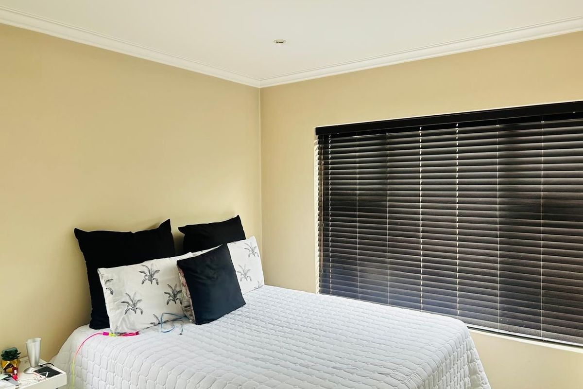 A well-lit bedroom featuring neutral wall tones, fitted venetian blinds, and recessed ceiling lighting, providing a comfortable and functional sleeping space.