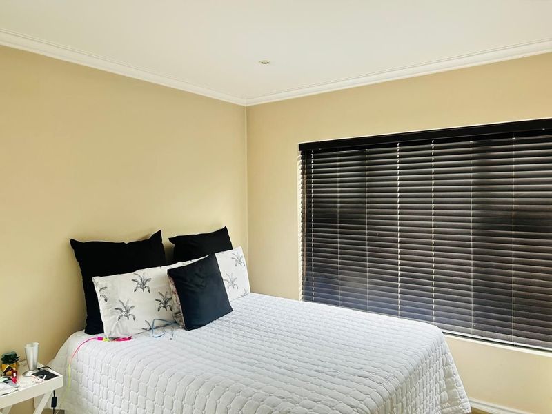 A well-lit bedroom featuring neutral wall tones, fitted venetian blinds, and recessed ceiling lighting, providing a comfortable and functional sleeping space.