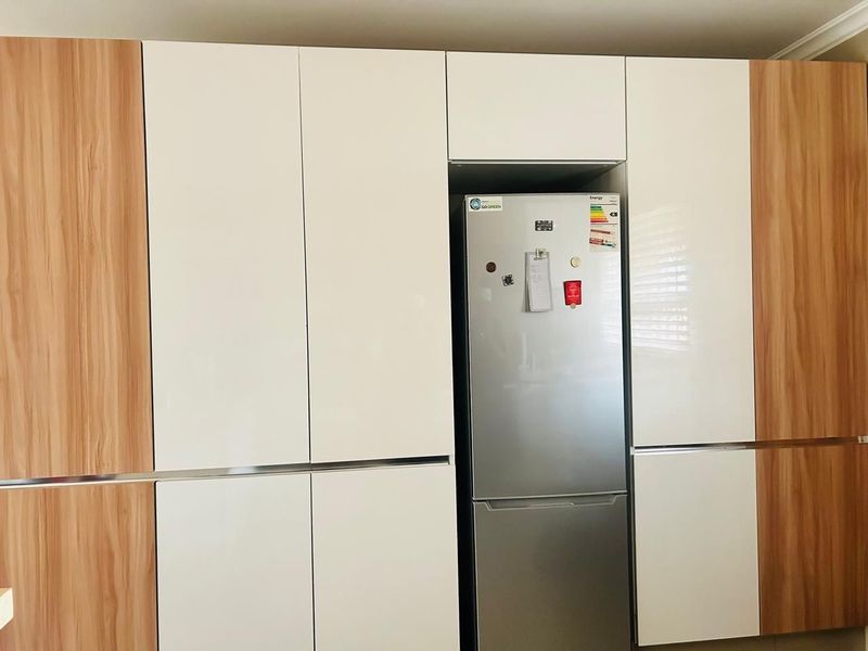 Modern kitchen featuring sleek, high-gloss white cabinetry accented with wood-grain panels and a dedicated integrated fridge housing unit.