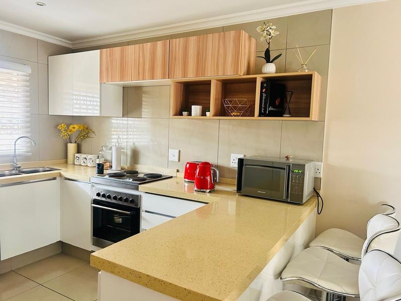 Modern kitchen featuring white and wood-grain cabinetry, stone countertops, integrated oven and hob, and a breakfast bar area.