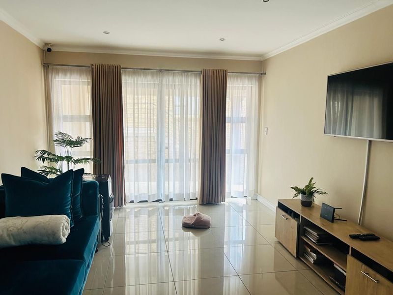 A bright living room featuring large sliding glass doors with curtains, polished tiled flooring, and recessed downlighting.