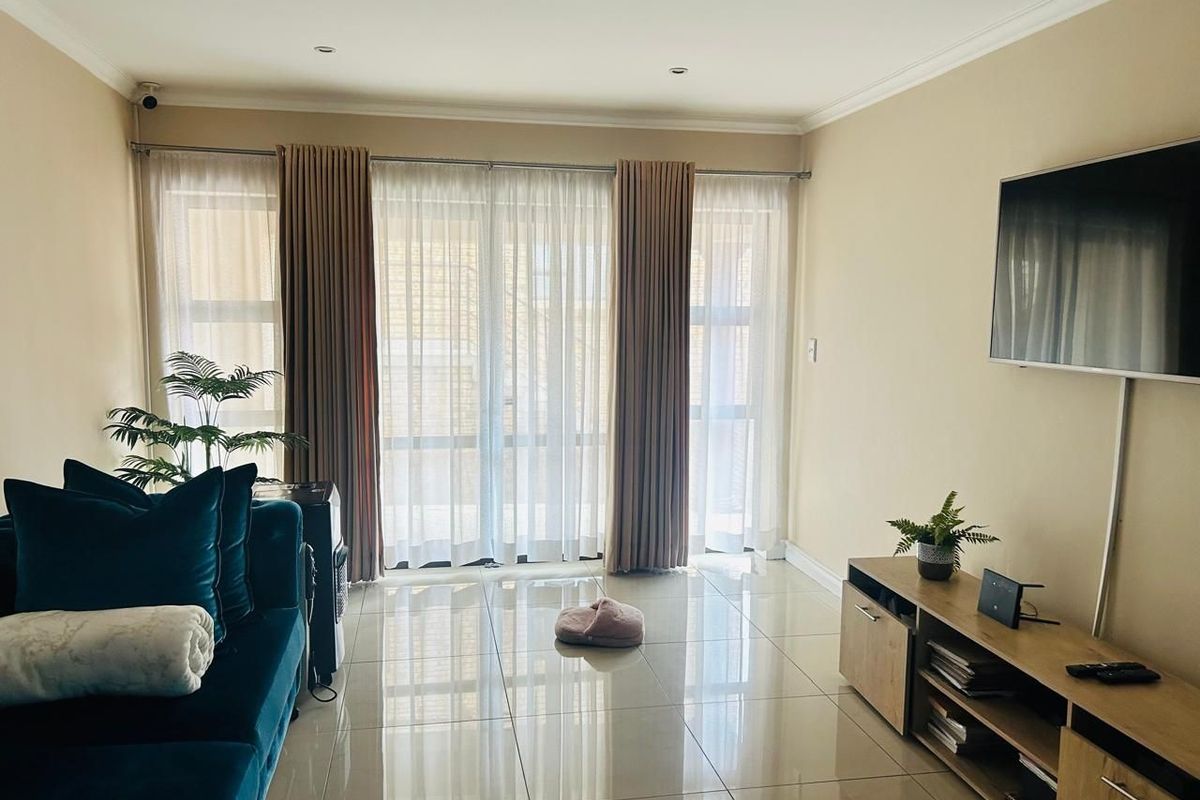 A bright living room featuring large sliding glass doors with curtains, polished tiled flooring, and recessed downlighting.