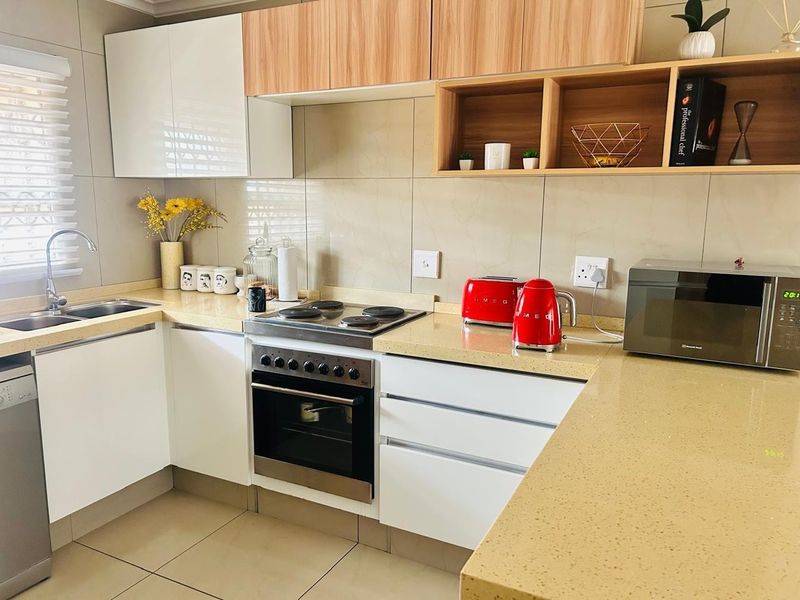 Modern kitchen featuring sleek white and wood-tone cabinetry, stone countertops, integrated electric hob and oven, and neutral tiled finishes throughout.