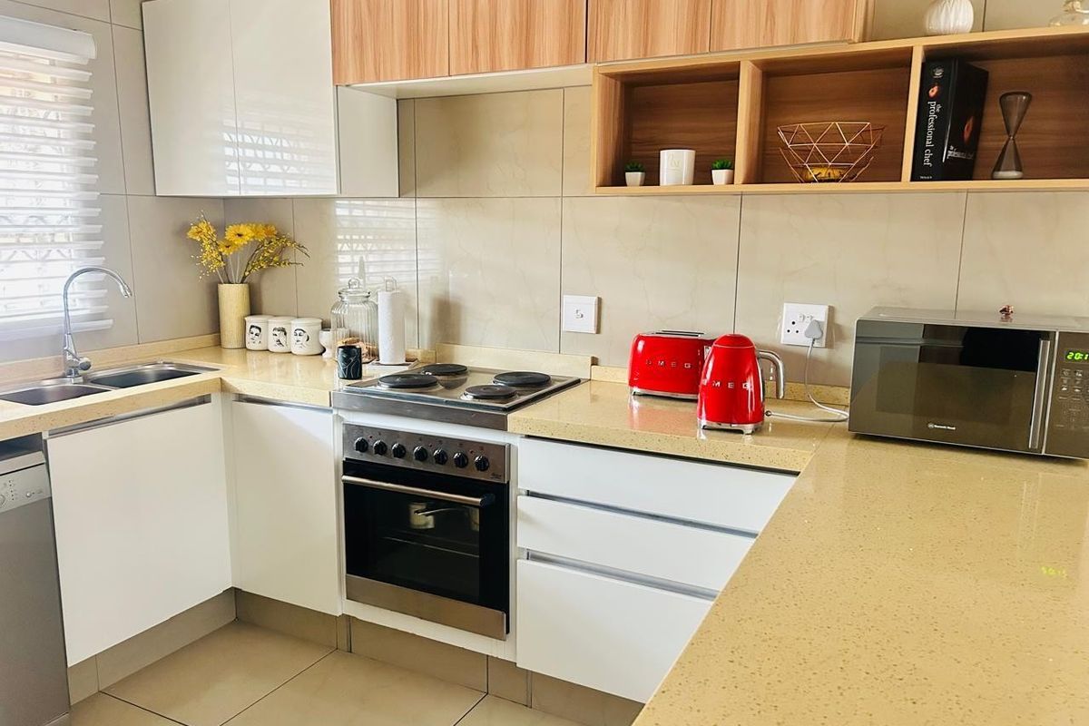 Modern kitchen featuring sleek white and wood-tone cabinetry, stone countertops, integrated electric hob and oven, and neutral tiled finishes throughout.