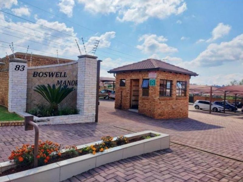 The entrance to Boswell Manor featuring a brick security guard house, paved driveway, and secure perimeter fencing.