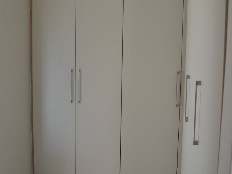 A clean and modern bedroom space featuring neutral-toned built-in cupboards with sleek handles and light-colored tiled flooring.