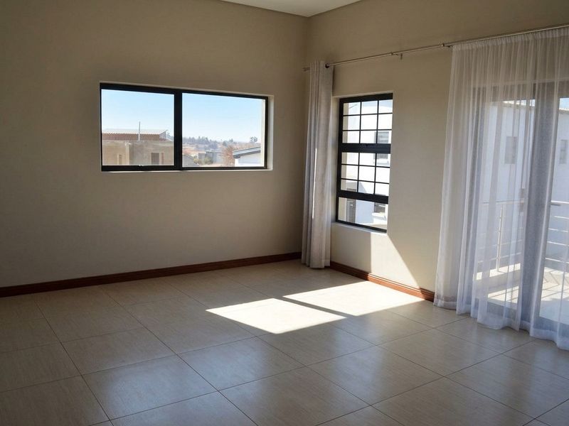 A bright, empty bedroom featuring neutral tiled flooring, large aluminium-framed windows, and a sliding door providing access to a balcony.