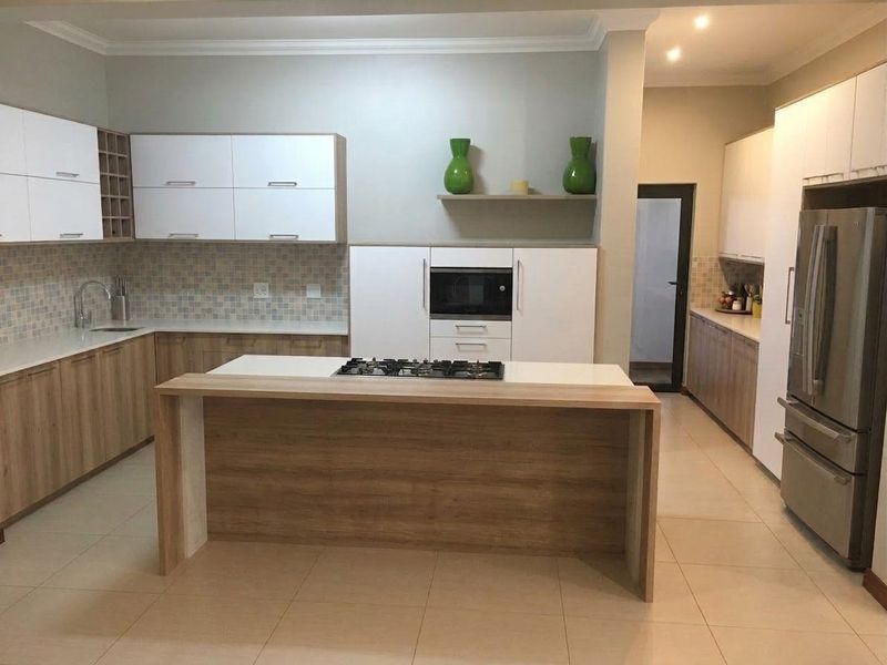 Modern kitchen featuring a central island with integrated gas hob, ample built-in cabinetry, mosaic tile backsplash, and high-quality finishes throughout.
