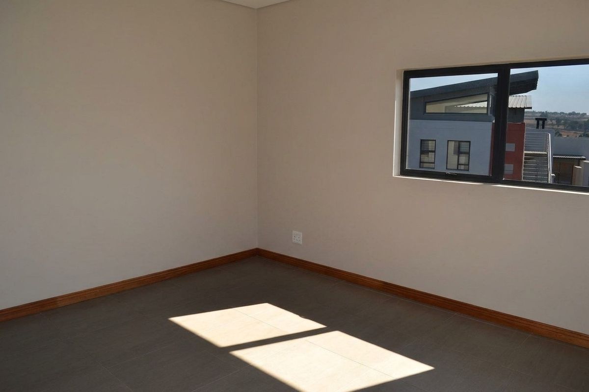 A bright, empty bedroom featuring neutral wall tones, tiled flooring, timber skirting boards, and an aluminium-framed window.