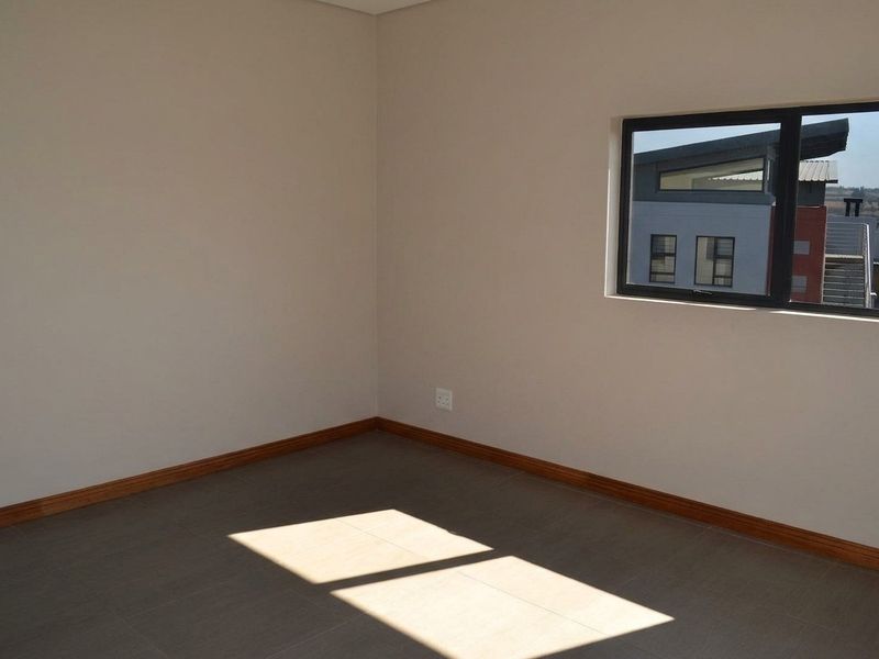 A bright, empty bedroom featuring neutral wall tones, tiled flooring, timber skirting boards, and an aluminium-framed window.