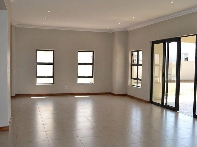 A spacious, empty living area featuring neutral tiled flooring, recessed downlighting, and large sliding glass doors providing access to the outdoor space.