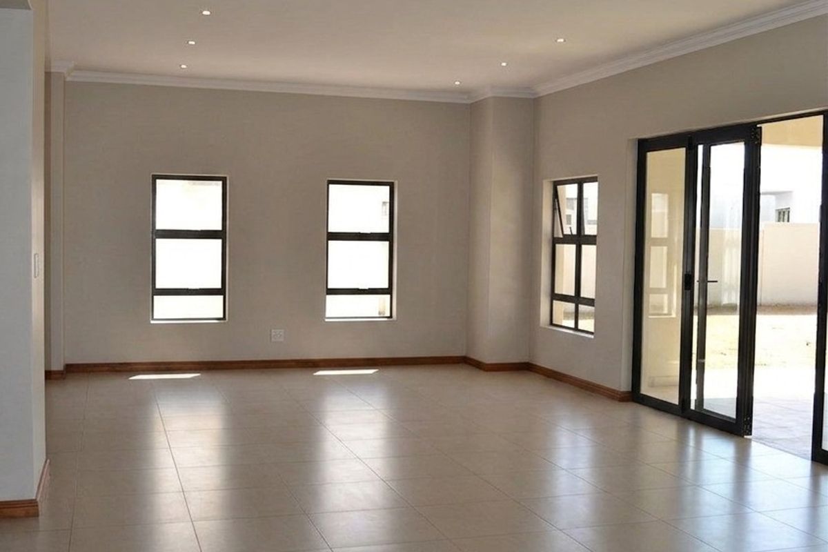 A spacious, empty living area featuring neutral tiled flooring, recessed downlighting, and large sliding glass doors providing access to the outdoor space.
