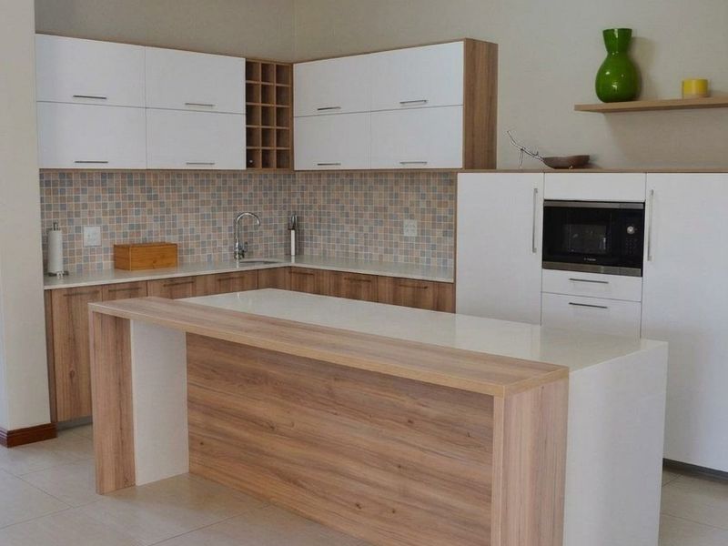 Modern kitchen featuring two-tone cabinetry, a central island with stone countertop, mosaic tile backsplash, and integrated microwave.