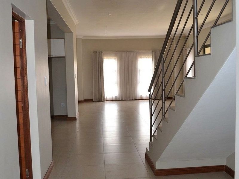 Spacious open-plan hallway featuring tiled flooring and a modern staircase with a stainless steel balustrade, leading into a bright, vacant living area.
