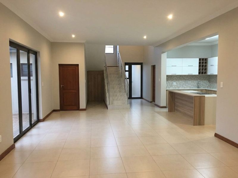 Spacious open-plan living area featuring tiled floors, recessed lighting, a modern staircase, and a functional kitchen with built-in cabinetry and an island.