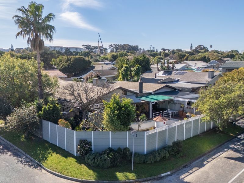 Aerial view of a residential corner property featuring a tiled roof, perimeter wall, and outdoor patio area within a suburban neighborhood setting.