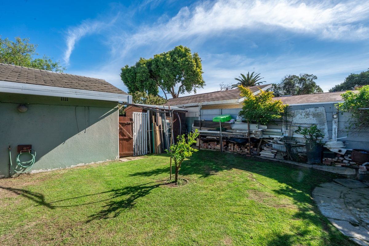 Rear garden area featuring a lawn, paved pathway, and external storage space, requiring maintenance and landscaping improvements.