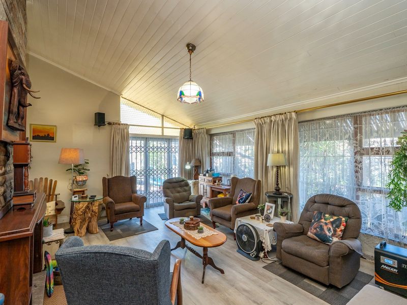Spacious living room featuring a stone fireplace, vaulted timber-clad ceiling, and laminate flooring, with direct access to the outdoor area through security gates.