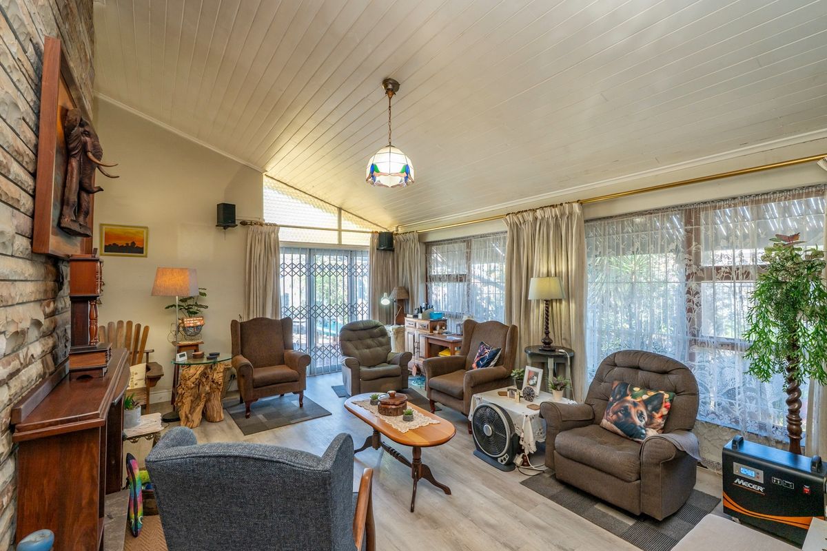 Spacious living room featuring a stone fireplace, vaulted timber-clad ceiling, and laminate flooring, with direct access to the outdoor area through security gates.