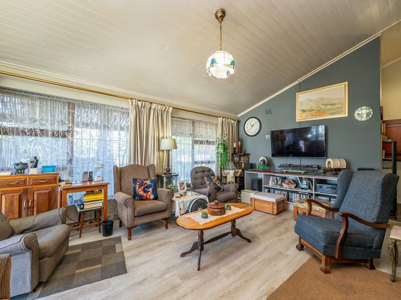 A comfortable living room featuring vaulted timber-paneled ceilings, light-toned laminate flooring, and large windows that provide ample natural light.