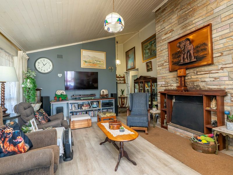 A cozy living room featuring a prominent stone fireplace with a timber mantelpiece, vaulted tongue and groove ceilings, and modern laminate flooring.