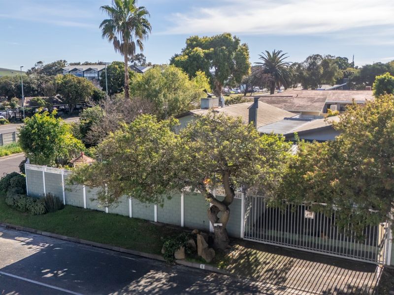 Aerial view of the property showing the street-facing perimeter wall, metal gate, and roof structure within a suburban neighborhood setting.