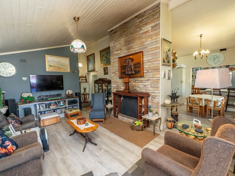 Open plan living and dining area featuring a prominent stone fireplace, timber mantelpiece, and light-toned laminate flooring under a high tongue and groove ceiling.