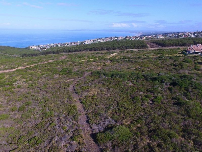 An aerial view of a large, undeveloped residential plot featuring natural coastal vegetation and scenic ocean views in the distance.