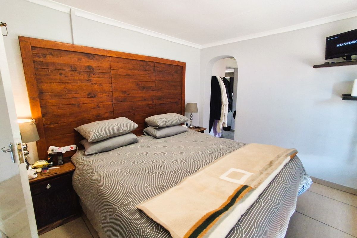 A bedroom featuring a large wooden headboard, tiled flooring, and an arched doorway leading to an adjacent space.