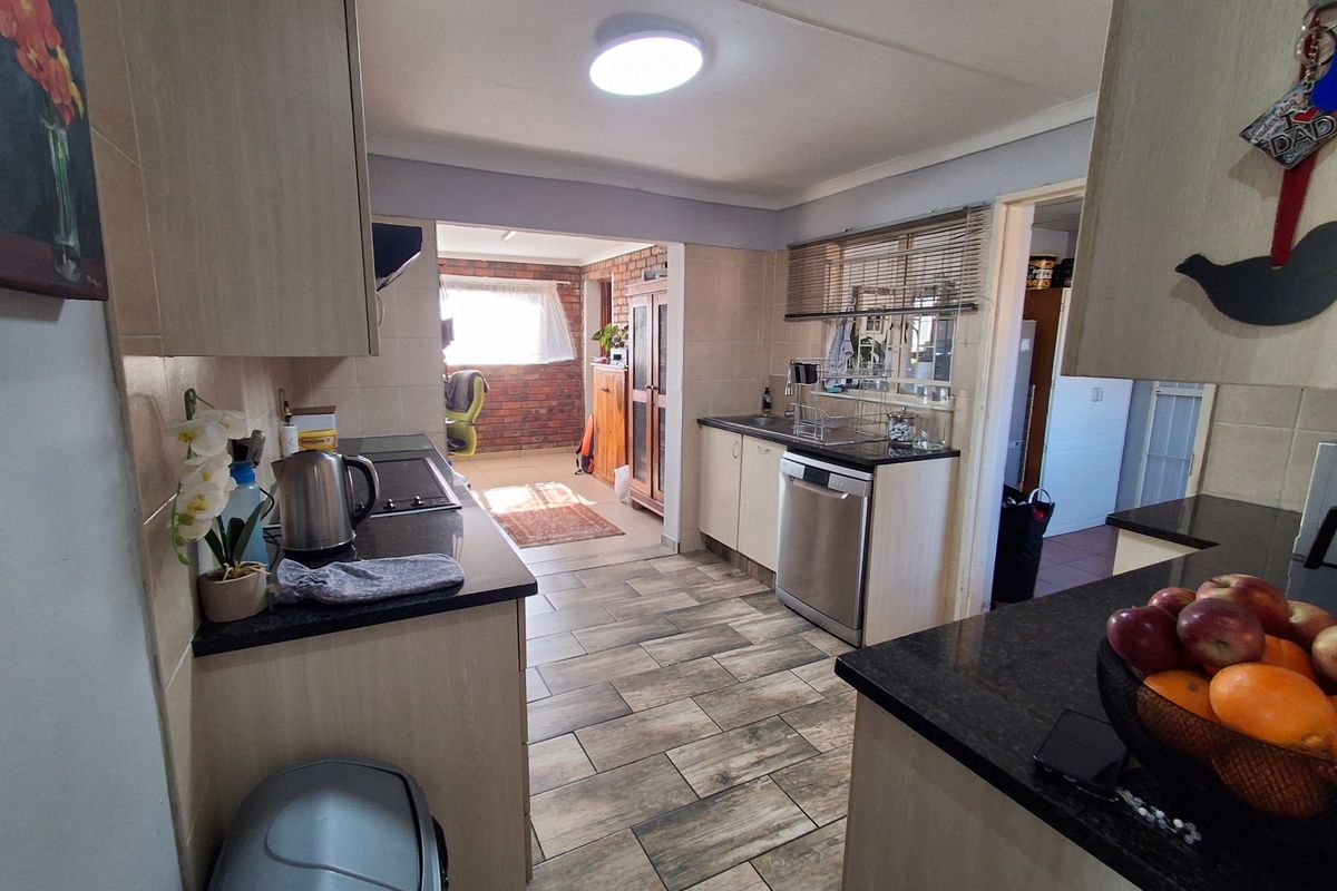 Functional kitchen featuring built-in cabinetry, granite countertops, tiled backsplash, and durable tiled flooring, with an open-plan layout leading to an adjacent living area.
