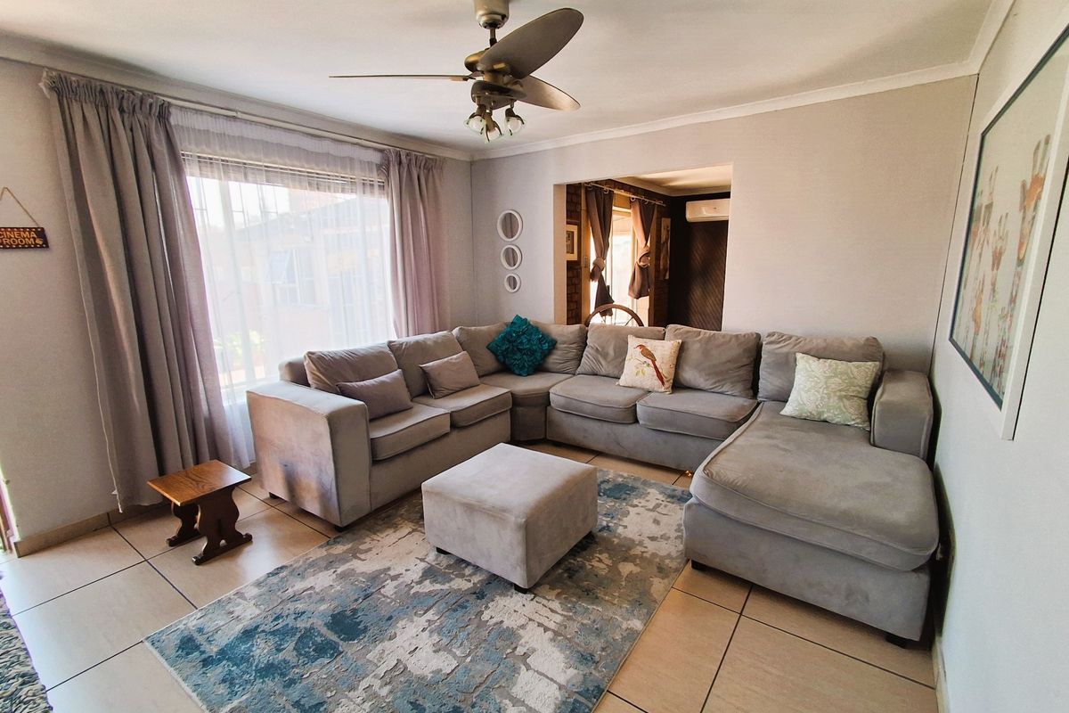 A comfortable living room featuring tiled flooring, a ceiling fan, and large windows with curtain tracks, offering a functional and well-lit space.