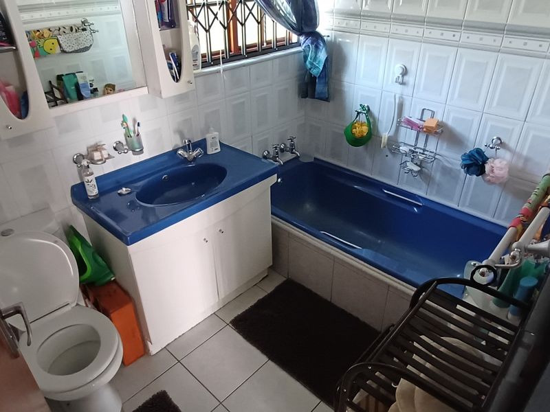 A functional bathroom featuring a blue vanity basin and matching bathtub, complemented by full-height wall tiling and tiled flooring.