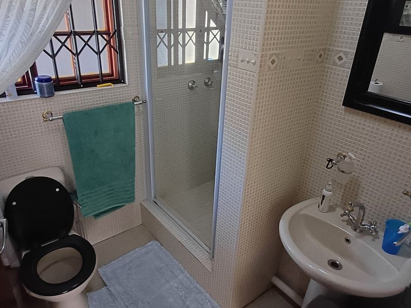 Compact bathroom featuring a pedestal basin, shower enclosure, and toilet with tiled wall finishes and security bars on the window.