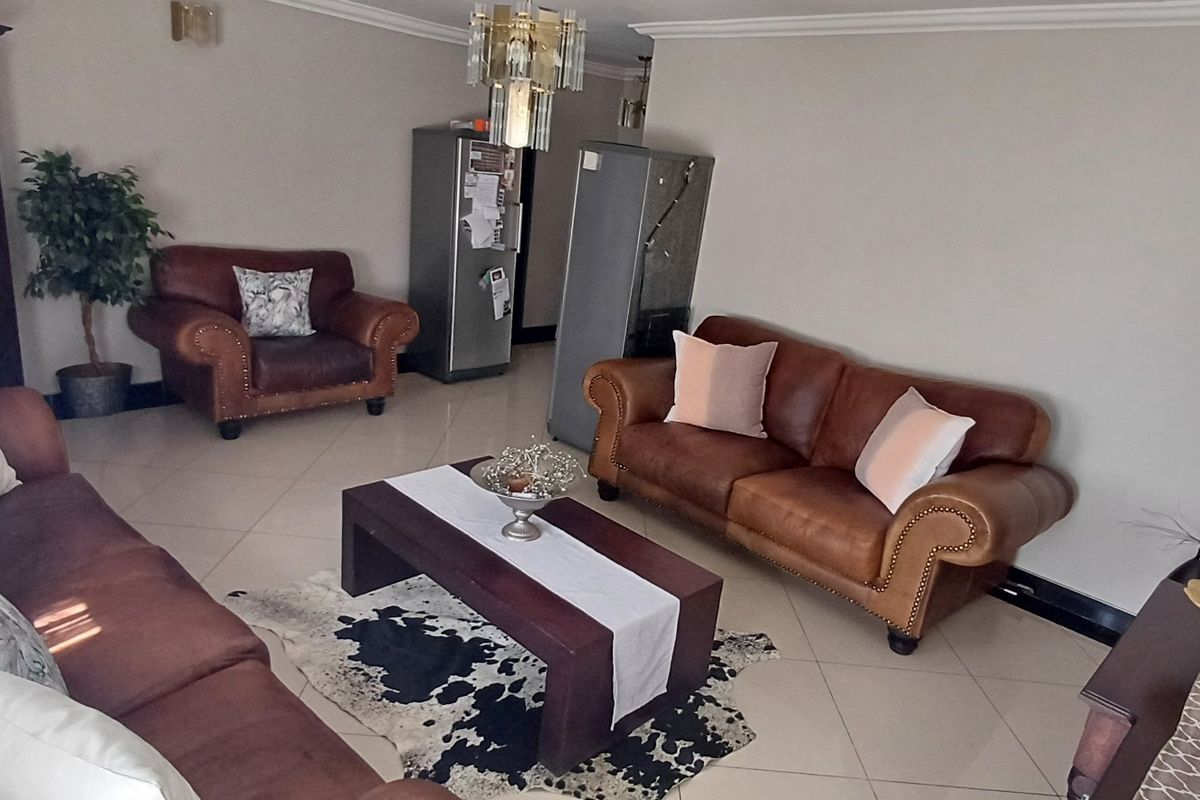A spacious living room featuring neutral tiled flooring, crown molding, and a central chandelier, providing a comfortable and well-lit area for relaxation.