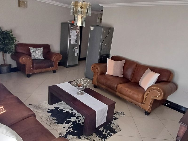 A spacious living room featuring neutral tiled flooring, crown molding, and a central chandelier, providing a comfortable and well-lit area for relaxation.