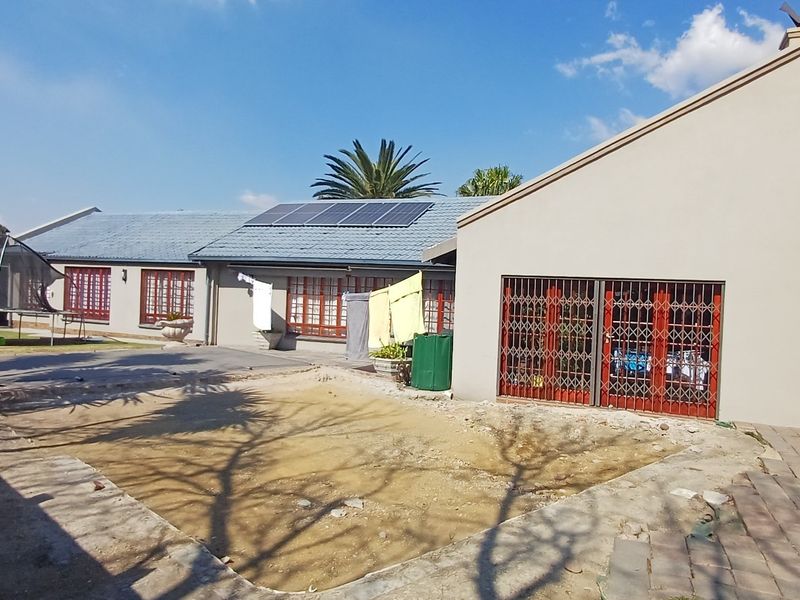 Rear exterior view of the house featuring a paved patio area, security gates, and roof-mounted solar panels with an unlandscaped garden section.