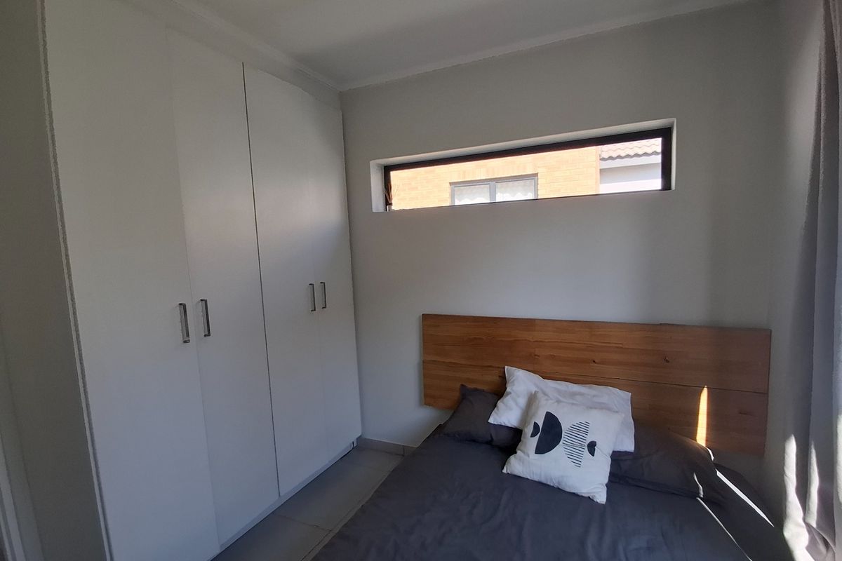 A modern bedroom featuring built-in white cupboards and a high-set clerestory window providing natural light.