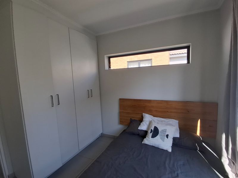 A modern bedroom featuring built-in white cupboards and a high-set clerestory window providing natural light.