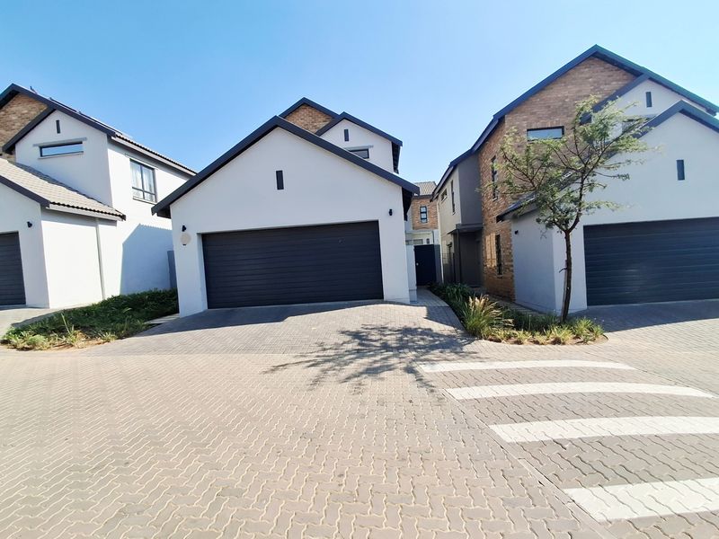 Front view of a modern residential property featuring a paved driveway, double garage, and contemporary architectural design with brick and plaster finishes.