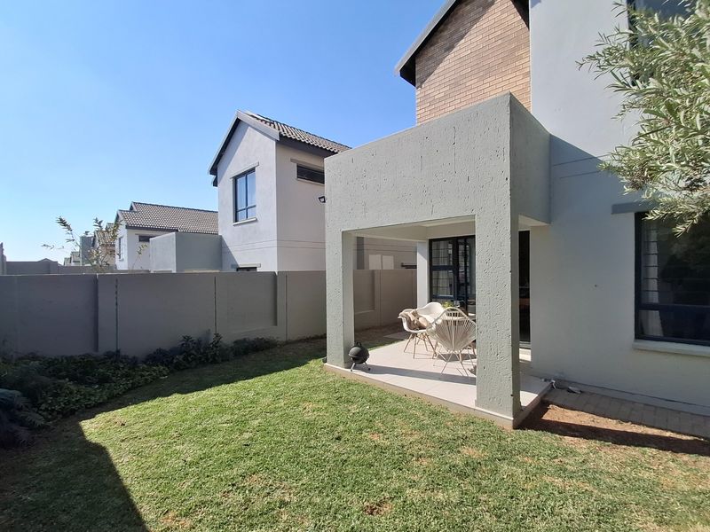 A rear view of the property featuring a covered patio area, tiled flooring, and a well-maintained private garden with boundary walls.