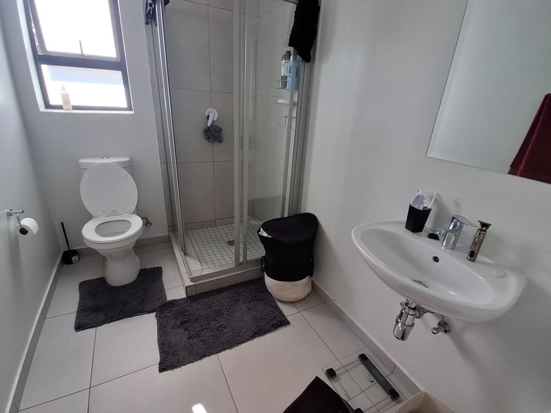 A functional bathroom featuring a glass shower enclosure, wall-mounted basin with mixer tap, and a standard toilet with tiled flooring.