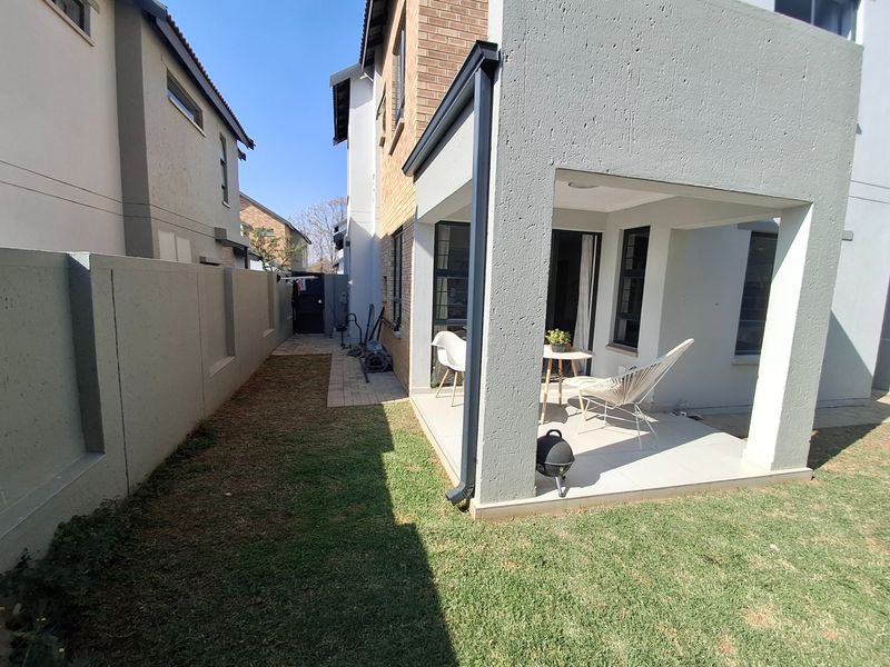 A covered patio area with tiled flooring, adjacent to a small private garden and side walkway, featuring modern brick and rendered exterior finishes.
