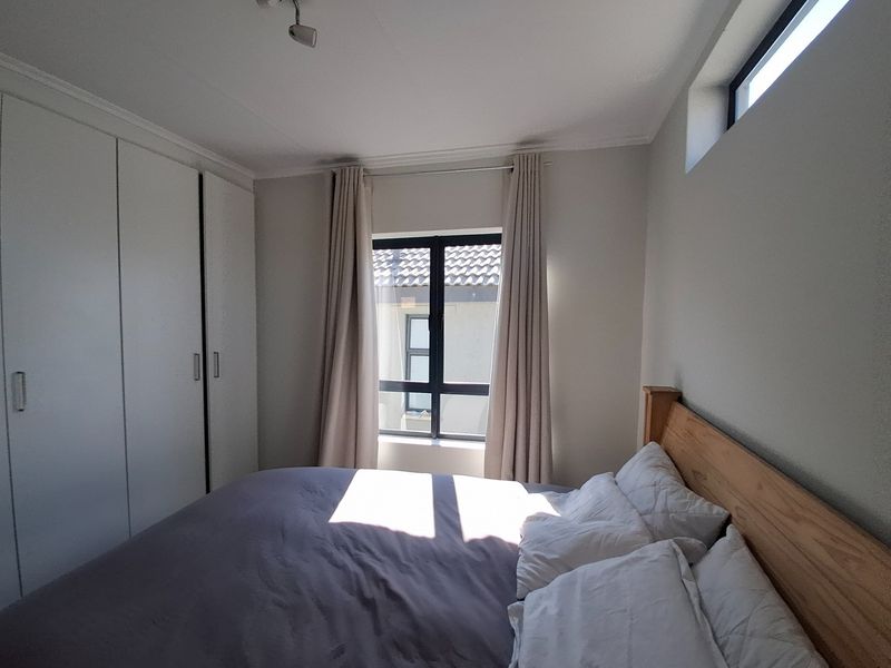A well-lit bedroom featuring built-in cupboards, neutral wall finishes, and a combination of standard and clerestory windows providing natural light.