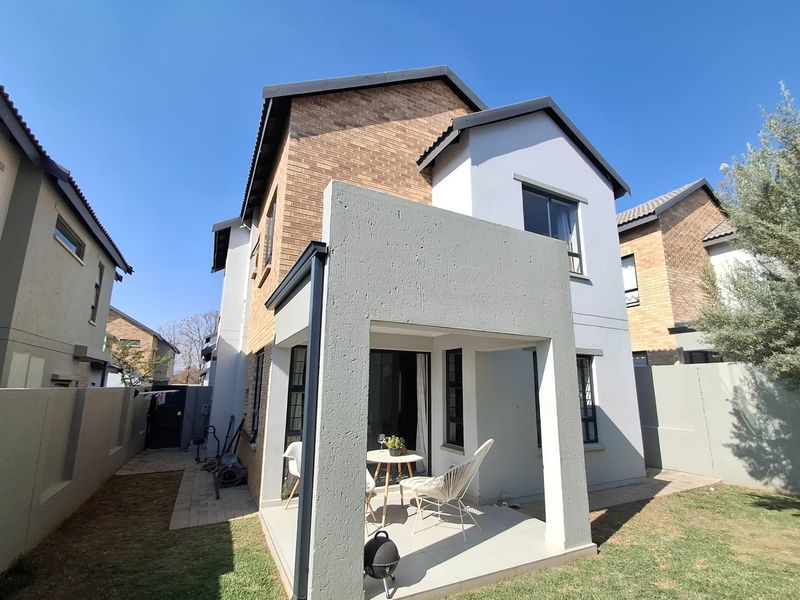 Rear view of a two-story residential house featuring a covered patio with tiled flooring and access through sliding glass doors.